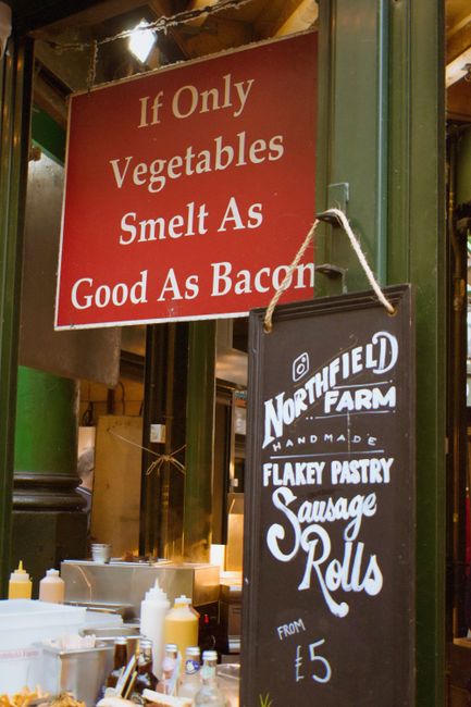 A close-up image of a market stall or local shop interior displaying a red sign that reads 'If Only Vegetables Smelt As Good As Bacon' and a black chalkboard sign advertising Northfield Farm's handmad