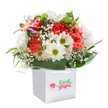 Radiating cheerful elegance, this lush bouquet in a pristine white square gift bag offers a little piece of Ealing's spirited charm. The arrangement bursts with the soft hues of coral, peach, and vibrant red carnations-their ruffled petals brimming with texture and life-nestled alongside crisp white daisies, each with a glowing yellow-green center that brings an inviting brightness. Wispy clouds of white baby's breath weave gentle threads between the larger blooms while hints of purple-tinged buds peep through, hinting at stories yet to unfold, as you might find in the quiet corners of Ealing's leafy lanes. Encircling all are bold, glossy green leaves, their lushness giving the bouquet a sense of fullness and generous welcome, like the embrace of a favorite local garden. Tied together and presented in the sleek gift bag with practical ribbon handles, it's a bouquet crafted to lift the spirit-perfect for marking a birthday, congratulating a friend, or simply lighting up a nearby home. Each carefully placed flower reflects the artistry and warmth that Ealing's florists bring to every occasion, ensuring this floral gift arrives as fresh as a morning in the borough itself.